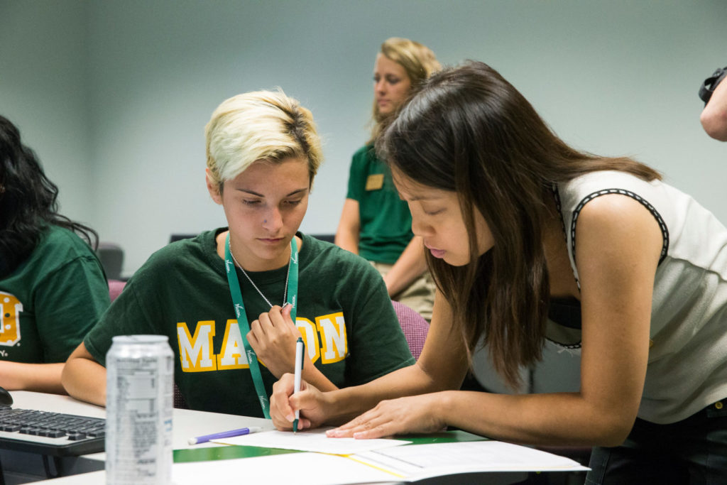 A UNIV Peer Advisor helps a student wearing a Mason sweatshirt with a worksheet in a UNIV 100 class.